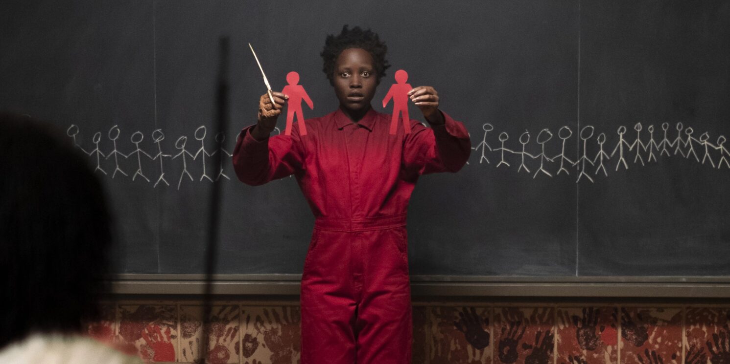 US (2019) Red (played by Lupita Nyong'o) Holding Paper Cut Outs of People with a crazed haunted expression on her face.