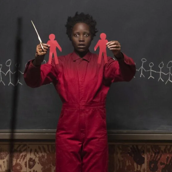 US (2019) Red (played by Lupita Nyong'o) Holding Paper Cut Outs of People with a crazed haunted expression on her face.