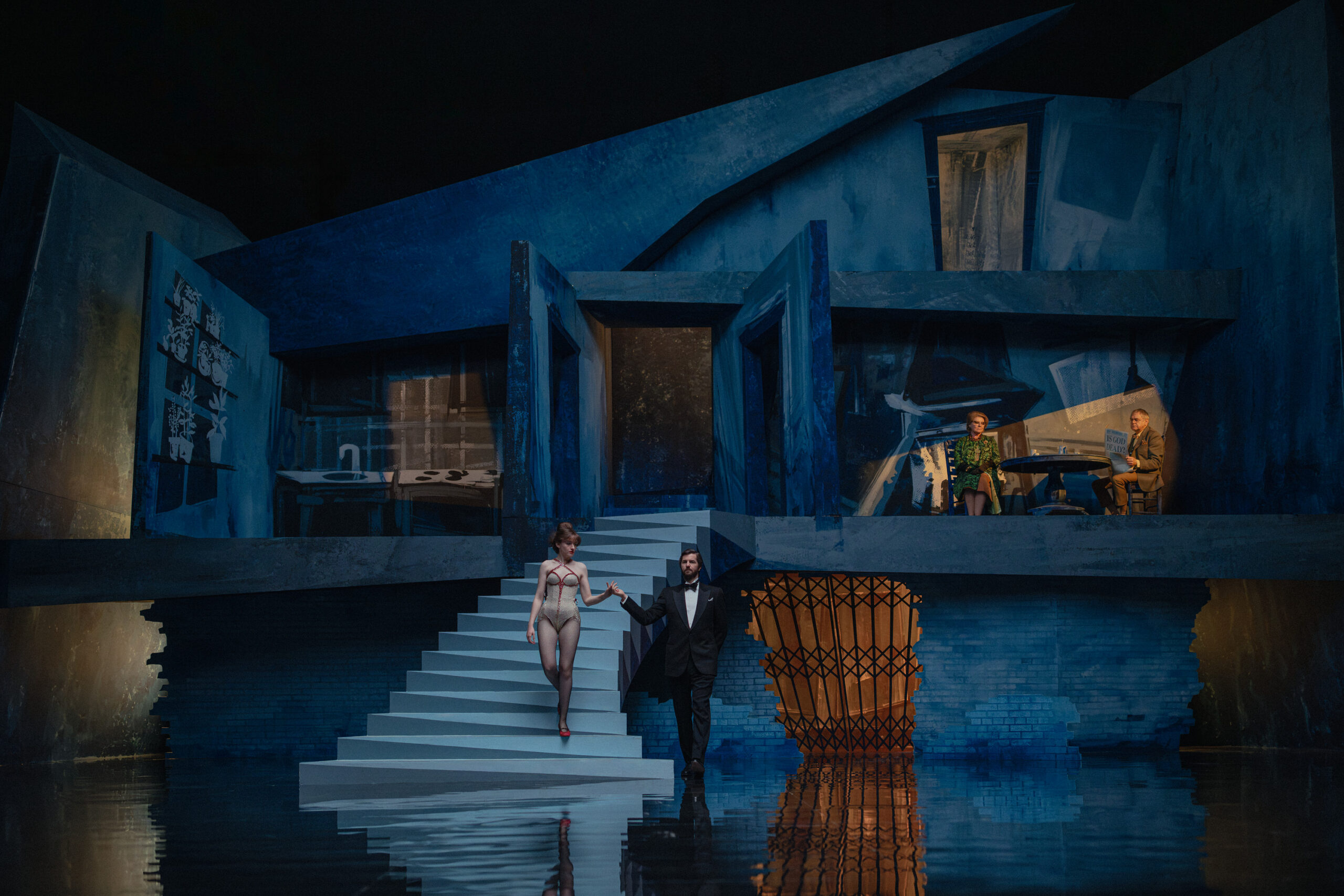 L-R Julia Garner as Terry Gionoffrio and Jim Sturgess as Alan Marchand in Apartment 7A, taking the final steps down a staircase into a strange stage set that look like a german expressionist interpretation of their apartment building