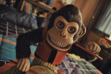 The Monkey (2025) - The Monkey Doll Bangs on His Drum with his creepy eyes wide open, baring his porcelain teeth