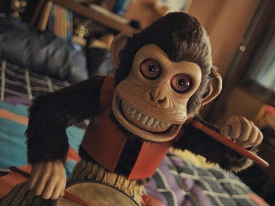 The Monkey (2025) - The Monkey Doll Bangs on His Drum with his creepy eyes wide open, baring his porcelain teeth